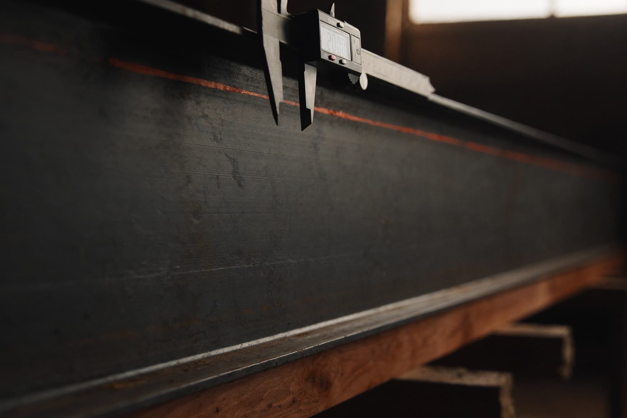 A digital caliper clamped over the edge of a large structural steel beam in a fabrication shop
