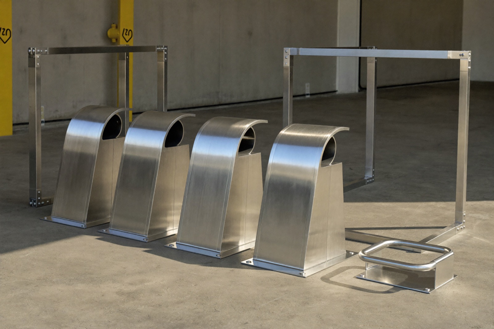 Formed stainless cowls and welded tube frames staged on a workshop floor in low raking light