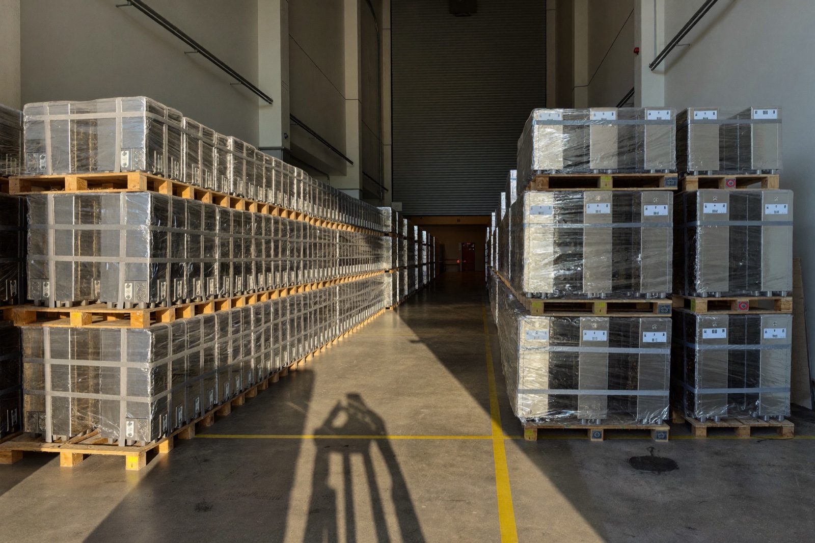 Wrapped and banded pallets of finished stainless units in long rows down a warehouse staging bay